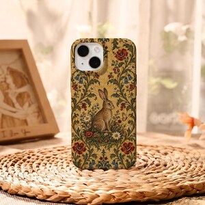 May include: A smartphone case featuring a repeating pattern of a brown rabbit surrounded by red poppies, blue bellflowers, and green foliage on a golden yellow background. The design includes a small butterfly and intricate floral vines.