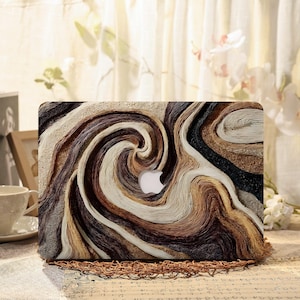 Peut inclure: Un autocollant pour ordinateur portable présentant un motif abstrait texturé et tourbillonnant dans des tons brun foncé, beige, crème et noir. Le design imite des lignes topographiques ou du bois, avec une découpe centrale révélant le logo Apple.