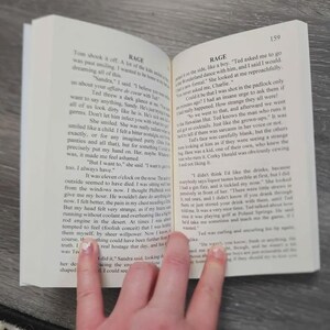 Puede incluir: Un libro abierto con p&aacute;ginas blancas y texto impreso en negro. La p&aacute;gina de la izquierda est&aacute; titulada RAGE y contiene varios p&aacute;rrafos de prosa narrativa. La p&aacute;gina de la derecha tambi&eacute;n est&aacute; titulada RAGE y muestra el n&uacute;mero de p&aacute;gina 159.