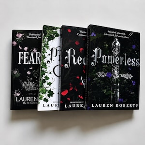 May include: Four hardcover books by Lauren Roberts arranged side-by-side. The covers feature dark, botanical, and metallic designs with titles including Fearless, Reckless, and Powerless in silver lettering against black, white, and red backgrounds.