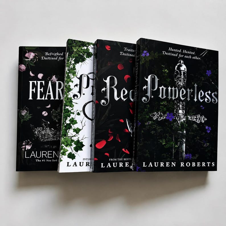 May include: Four hardcover books by Lauren Roberts arranged side-by-side. The covers feature dark, botanical, and metallic designs with titles including Fearless, Reckless, and Powerless in silver lettering against black, white, and red backgrounds.