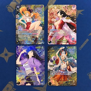 May include: Four One Piece trading cards featuring Nami, Boa Hancock, Nico Robin, and Yamato. Each card displays a character illustration with gold foil accents, a 5000 power rating, and a 01/50 serial number printed on a holographic background.