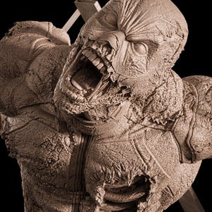 May include: A monochromatic brown sculpture of a humanoid figure with a textured, weathered surface. The figure has an open mouth revealing teeth, a mask-like head covering, and a torso with exposed rib-like structures and tattered details.
