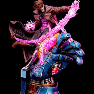 May include: A collectible statue of a character with brown hair wearing a brown trench coat and purple shirt, standing on a large blue mechanical gauntlet. The figure holds a playing card with a pink energy effect and glowing pink light trails.
