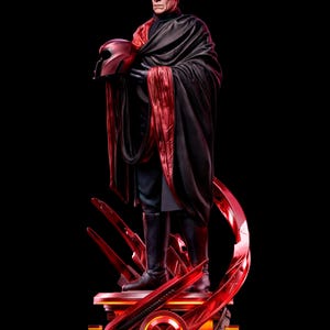 May include: A detailed collectible statue of an older man with gray hair, wearing a black outfit and a long black cape with a red lining. He holds a red helmet in his hand. The figure stands on a circular red base featuring an X-shaped emblem.