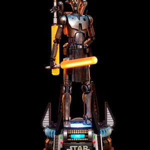 May include: A metallic droid figurine standing on a circular base with the Star Wars logo. The droid features a weathered silver finish, glowing orange eyes, and holds a bright orange light-up staff. The base includes blue and red accent lights.