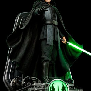 May include: A detailed action figure of a character wearing a black hooded cloak, black tunic, and black boots. The figure holds a glowing green lightsaber in one hand and stands on a mechanical base featuring a circular, illuminated green Jedi symbol.