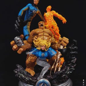 Peut inclure: Une statue de collection Fantastic Four représentant Mr. Fantastic, La Chose tenant un masque argenté, La Femme Invisible et La Torche Humaine dans une pose dynamique. La base présente un logo bleu numéro 4 sur un socle circulaire argenté.