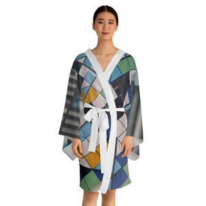 Pode incluir: Um roupão estilo quimono com um padrão geométrico de linhas e blocos que se cruzam em tons de azul, verde, amarelo e cinzento. A peça tem um rebordo branco sólido ao longo da abertura frontal e um cinto de tecido branco a condizer na cintura.