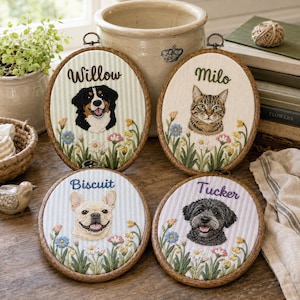 以下が含まれることがあります： ペットの刺繍ポートレートが施された4つの楕円形刺繍枠。2つはWillowとMiloという名前の縦型、2つはBiscuitとTuckerという名前の円形です。それぞれ、色とりどりの刺繍された野花の上にペットの顔がデザインされています。