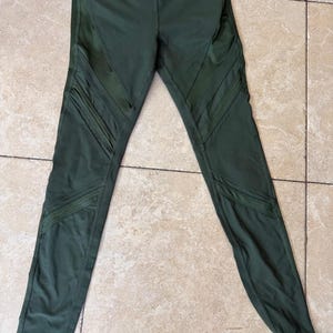 Peut inclure: Legging vert olive dot&eacute; d'une taille haute et d'empi&egrave;cements en maille diagonaux d&eacute;coratifs le long des cuisses et des mollets. Ce pantalon de sport pr&eacute;sente une silhouette ajust&eacute;e avec des coutures visibles et un tissu opaque et lisse.