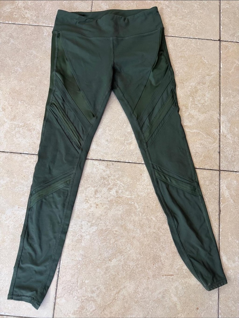 Peut inclure: Legging vert olive dot&eacute; d'une taille haute et d'empi&egrave;cements en maille diagonaux d&eacute;coratifs le long des cuisses et des mollets. Ce pantalon de sport pr&eacute;sente une silhouette ajust&eacute;e avec des coutures visibles et un tissu opaque et lisse.