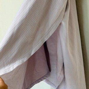 Peut inclure: Un v&ecirc;tement lilas clair pr&eacute;sentant une texture finement c&ocirc;tel&eacute;e et une fente lat&eacute;rale. Le tissu affiche un motif &agrave; rayures verticales coh&eacute;rent sur toute la surface, avec des coutures visibles le long de l'ourlet et de l'ouverture lat&eacute;rale.