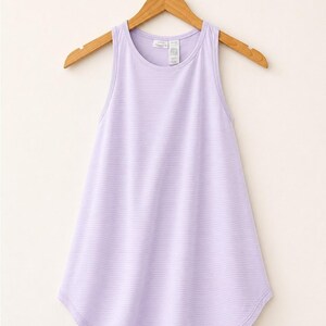 Peut inclure: Un d&eacute;bardeur sans manches violet clair avec un motif &agrave; fines rayures horizontales, une encolure ronde et un ourlet arrondi. Le v&ecirc;tement est pr&eacute;sent&eacute; sur un cintre en bois, r&eacute;v&eacute;lant une coupe simple avec une &eacute;tiquette de marque visible.