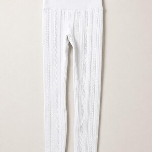 May include: A pair of white leggings featuring a vertical cable knit pattern throughout the legs and a wide, ribbed high-waist band. The leggings are displayed hanging from a black plastic hanger against a plain, light-coloured background.