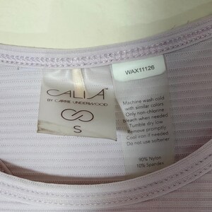 Peut inclure: Un haut c&ocirc;tel&eacute; lilas clair avec une &eacute;tiquette de marque Calia by Carrie Underwood, taille S, et une &eacute;tiquette d'entretien. Le v&ecirc;tement est compos&eacute; de 90 % de nylon et 10 % d'&eacute;lasthanne, avec le texte WAX11126 et des instructions de lavage.