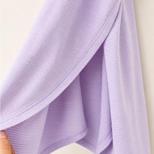 Peut inclure: Un v&ecirc;tement violet clair dot&eacute; d'une texture c&ocirc;tel&eacute;e et d'une fente lat&eacute;rale. Le tissu pr&eacute;sente un motif c&ocirc;tel&eacute; horizontal uniforme sur toute la surface, avec un ourlet net le long de l'ouverture de la fente, r&eacute;v&eacute;lant la couleur lavande douce.
