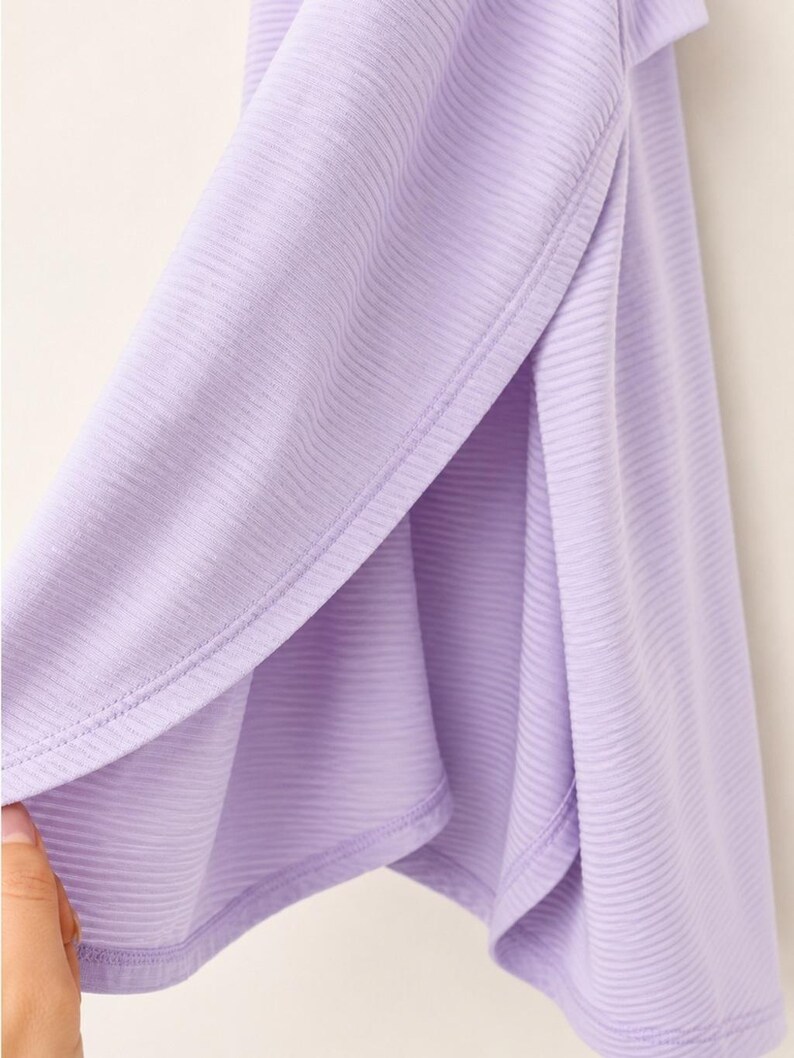 Peut inclure: Un v&ecirc;tement violet clair dot&eacute; d'une texture c&ocirc;tel&eacute;e et d'une fente lat&eacute;rale. Le tissu pr&eacute;sente un motif c&ocirc;tel&eacute; horizontal uniforme sur toute la surface, avec un ourlet net le long de l'ouverture de la fente, r&eacute;v&eacute;lant la couleur lavande douce.