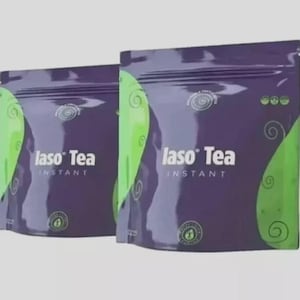 May include: Two purple and green pouches of Iaso Tea Instant. The packaging features the text Iaso Tea Instant in white, with swirling green graphic patterns on the sides and small circular logos printed on the front of each sealed bag.