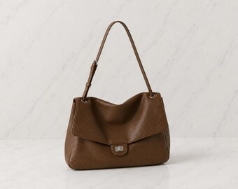 May include: A brown shoulder bag with a soft, slouchy silhouette, a wide fold-over flap, and a silver-toned metal turn-lock closure. The bag features a single adjustable shoulder strap attached with silver-toned hardware rings on each side.