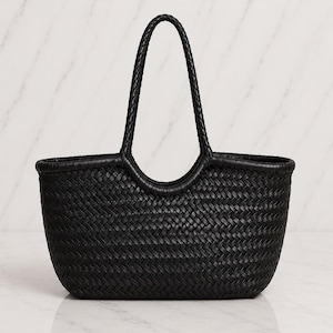 May include: A black tote bag featuring a woven construction with a consistent herringbone pattern throughout the body. The bag includes two integrated, braided handles that extend from the top edge, creating a rounded opening for carrying.