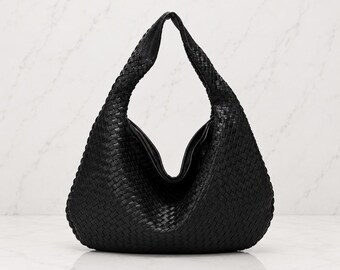 May include: A black hobo bag featuring an intricate woven leather pattern throughout the entire exterior. The bag has a single integrated shoulder strap that forms a triangular silhouette, with a deep, curved opening at the top center.