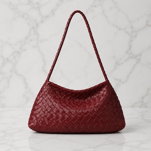 May include: A deep red shoulder bag featuring an intricate woven leather pattern throughout the body and a single, matching braided leather strap. The bag has a curved, structured silhouette with a wide base and a tapered top opening.
