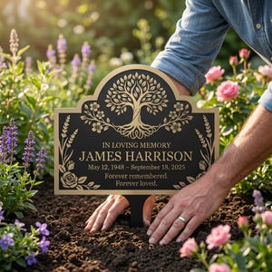 Puede incluir: Una placa conmemorativa negra y dorada con un diseño grabado del árbol de la vida, detalles florales y el texto: IN LOVING MEMORY JAMES HARRISON May 12, 1948 – September 18, 2025 Forever remembered. Forever loved. La placa incluye una estaca para el suelo.
