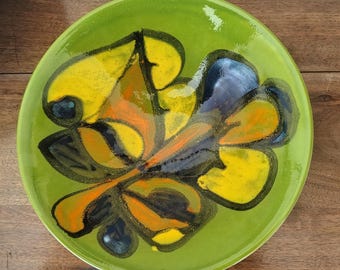 Może przedstawiać: Okrągły talerz ceramiczny z błyszczącym, limonkowym szkliwem. W centrum znajduje się abstrakcyjny, ręcznie malowany wzór z wyraźnymi czarnymi konturami wypełnionymi żywymi plamami żółci, pomarańczu i głębokiego błękitu, tworzącymi kształt liścia.