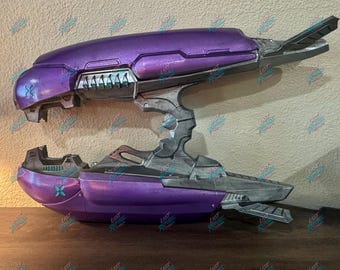 Könnte beinhalten: Eine violette und metallisch graue Sci-Fi-Plasma-Gewehr-Requisite mit einem geteilten Laufdesign, bei dem zwei separate Abschnitte durch eine zentrale Stützstruktur verbunden sind. Die Waffe hat türkisfarbene Akzente und kantige Paneele.