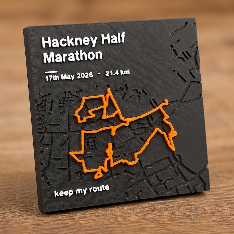 May include: A square black plaque featuring a raised white map of the Hackney Half Marathon route with orange path detailing. Text includes Hackney Half Marathon, 17th May 2026, 21.4 km, and keep my route. The surface has a textured, matte finish.
