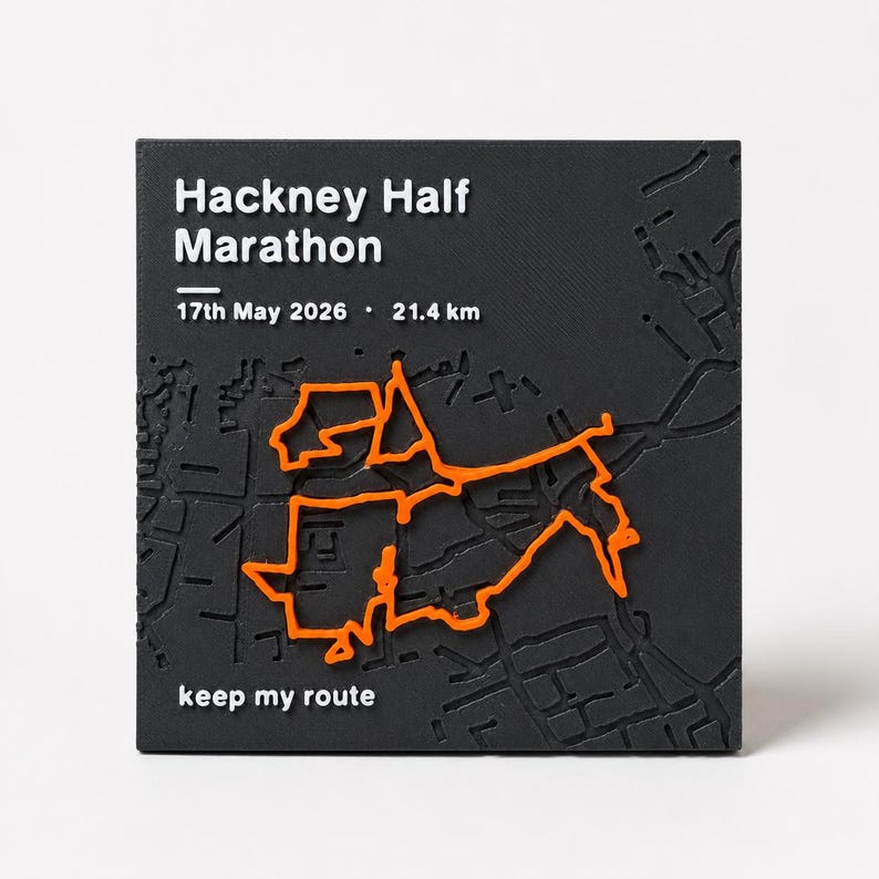 May include: A square black plaque featuring a raised orange map route of the Hackney Half Marathon. The text reads Hackney Half Marathon, 17th May 2026, 21.4 km, and keep my route. The surface displays a textured street grid in relief.