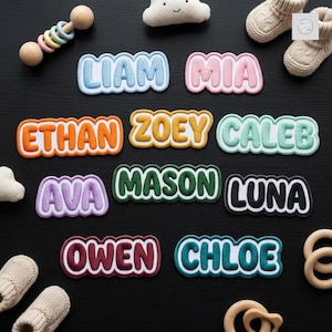 May include: A collection of ten embroidered name patches in various colors including light blue, pink, orange, yellow, mint green, purple, dark green, black, maroon, and teal, arranged with baby booties, a wooden rattle, and a cloud-shaped toy.