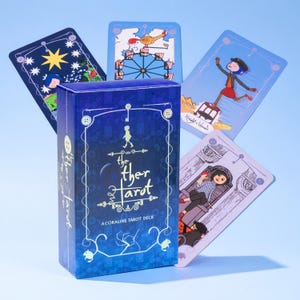Könnte beinhalten: Eine blaue, rechteckige Tarot-Kartenschachtel mit der Aufschrift The Other Tarot A Coraline Tarot Deck und weißen Strichzeichnungen von Knöpfen und einem Schlüssel. Vier illustrierte Tarotkarten sind fächerförmig hinter der Schachtel angeordnet.