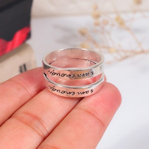 Peut inclure: Une bague en métal argenté composée de deux anneaux superposés. Chaque anneau est gravé du texte en cursive noire "i am enough" qui fait le tour de la surface extérieure. La bague présente une finition lisse et polie avec un design ouvert.