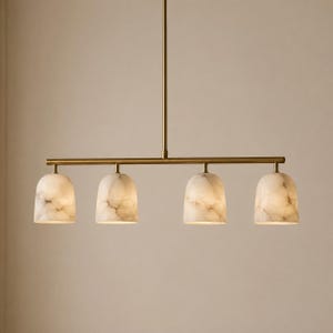 May include: A linear pendant light fixture featuring a long, thin brass-toned metal rod suspended from a single vertical stem. Four dome-shaped shades made of white and grey marbled stone are attached to the horizontal bar, emitting a soft glow.