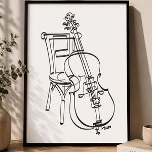 Peut inclure: Une impression d'art en noir et blanc dans un cadre noir représentant un dessin au trait continu d'un violoncelle appuyé contre une chaise en bois. L'œuvre est posée sur une surface à côté de deux livres avec le texte KINFOLK et THE KINFOLK HOME.