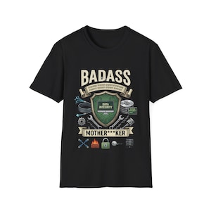 Puede incluir: Una camiseta negra de manga corta con un estampado gráfico que incluye el texto BADASS MOTHER***KER. El diseño presenta un escudo central con un monitor de ordenador que muestra DATA INTEGRITY, rodeado de código binario, herramientas e iconos.