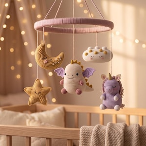 May include: A nursery mobile featuring a circular pink frame with hanging crocheted figures including a yellow crescent moon, a white star, a white dragon with purple wings, a white cloud with yellow dots, and a purple unicorn with a gold horn.