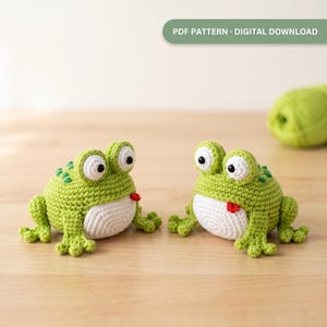 May include: Two crocheted green frogs with white bellies, large white eyes with black pupils, and small red tongues sticking out. The frogs have textured backs and webbed feet. The image includes the text PDF PATTERN - DIGITAL DOWNLOAD.