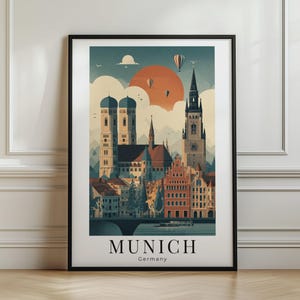 Pode incluir: Uma impressão artística emoldurada com uma ilustração estilizada do horizonte de Munique, Alemanha. A obra exibe edifícios históricos, torres de igrejas, um grande sol laranja e balões de ar quente no céu. O texto MUNICH Germany está impresso na parte inferior.