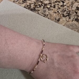 May include: A delicate bracelet featuring a series of small, alternating light-colored and dark-colored beads strung on a thin cord. A gold-toned metal charm shaped like an open, stylized heart hangs from the center of the beaded bracelet.