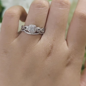 May include: A silver-toned ring set featuring a central cushion-shaped cluster of small clear stones, flanked by an intricate twisted band design. The ring is paired with a matching curved band encrusted with a row of tiny clear stones.
