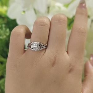 May include: A silver-toned ring featuring a square-shaped cluster of small clear stones at the center, flanked by intricate openwork metal detailing on the band, and paired with a thin, separate band encrusted with a row of tiny clear stones.