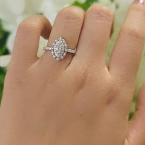 May include: A silver-toned ring featuring a central marquise-cut stone surrounded by a halo of smaller round stones. The band is thin and encrusted with tiny pavé-set stones along the shank, creating a bright, reflective, and detailed appearance.