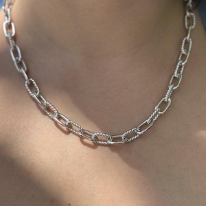 May include: A silver-toned chain necklace featuring alternating oval links. The design consists of smooth, polished oval links connected by textured, twisted rope-style oval links, creating a repeating pattern around the entire length of the necklace.