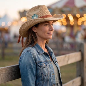 Peut inclure: Un chapeau en paille tressée beige orné d'une fleur crochetée bleu clair sur le côté et d'une bande texturée couleur rouille. Le chapeau présente un large bord et deux fins rubans couleur rouille pendants à l'arrière, porté avec une veste en jean.