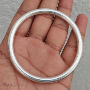 May include: A smooth, polished silver bangle bracelet with a rounded, circular profile. The metal surface is reflective and uniform in thickness, creating a simple, continuous loop design. The text "Boho Mystic Silver" is printed in the bottom left.