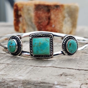 May include: A silver cuff bracelet featuring a central square turquoise stone and two smaller oval turquoise stones on either side. Each stone is set within a twisted silver wire border. The text Boho Mystic Silver is printed at the bottom.
