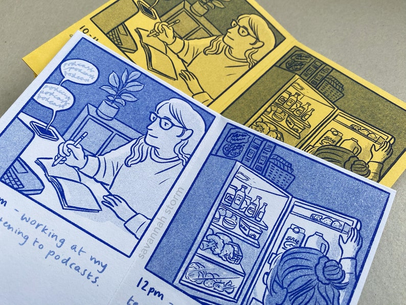 Two comic zines open on pages showing comic panels of a girl sitting at a desk drawing in a sketchbook, and a girl opening a fridge.